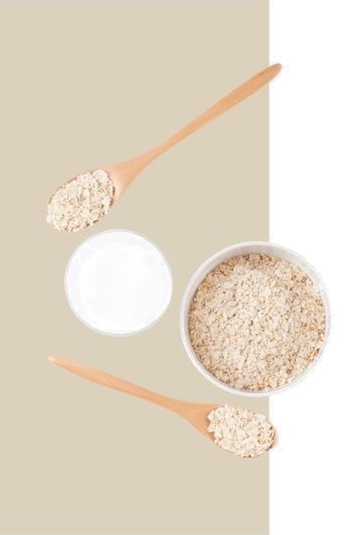 Wooden spoons and a bowl of rolled oats beside a dish of oat milk