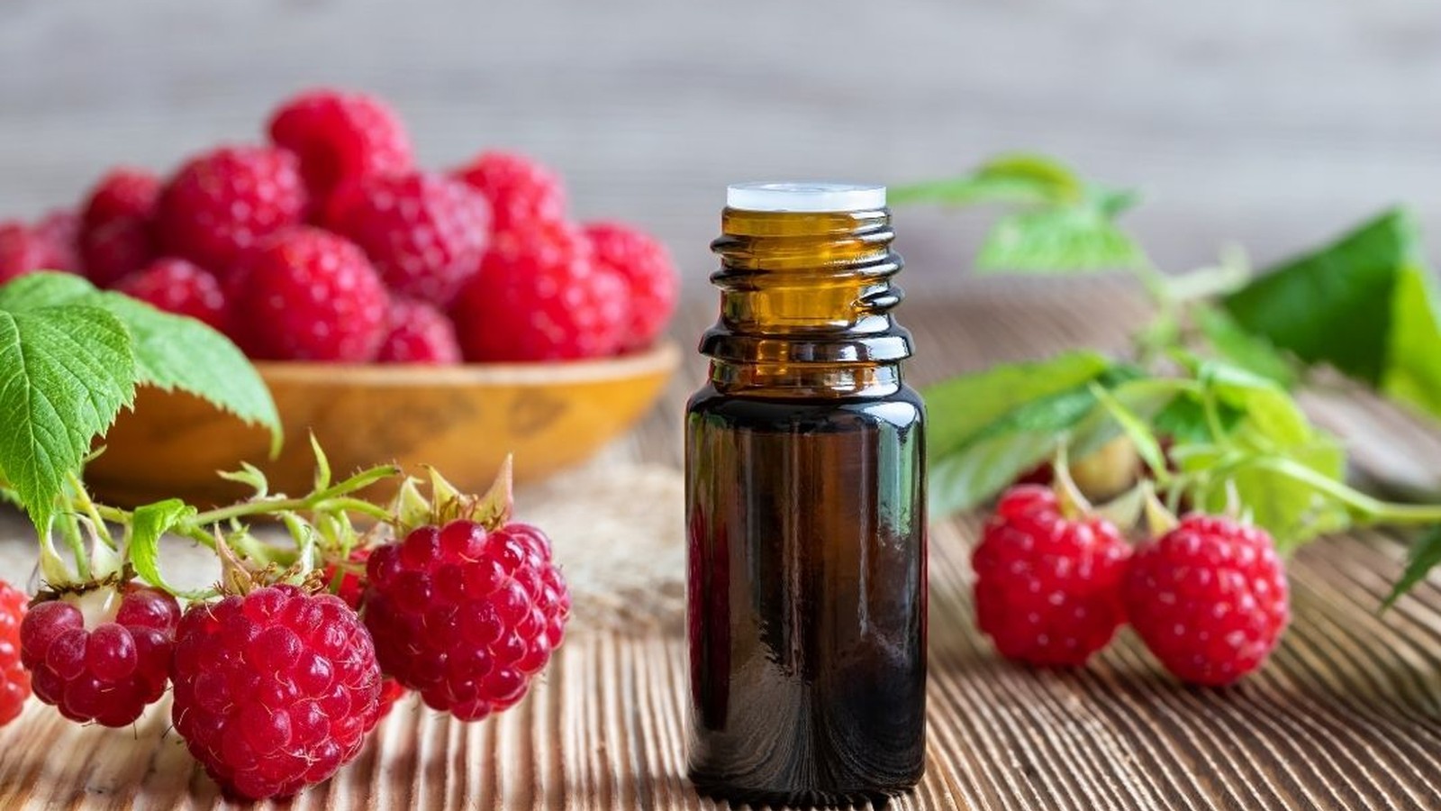 Amber bottle of raspberry seed oil beside fresh red raspberries and leaves