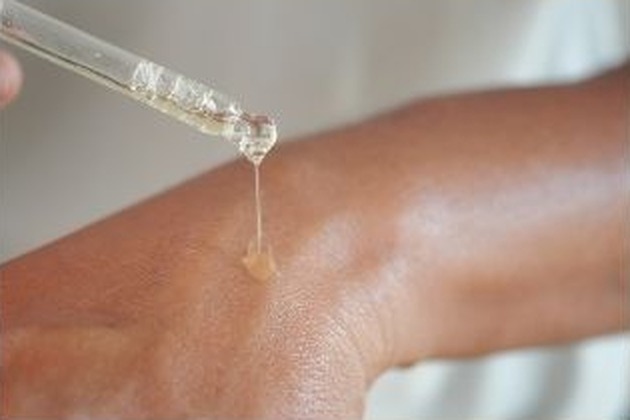 Drop of squalane falling from a glass dropper onto the back of a hand